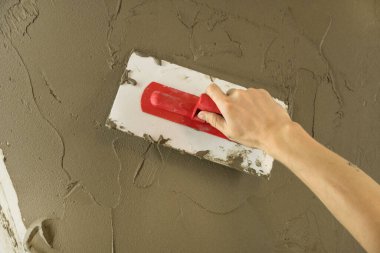 Bir işçi duvarı spatulayla kaplıyor ve çimento karışımı solüsyonu uyguluyor. Tamirci alçıpanı alçıpan üzerine serer. Tamirci evi tamir ediyor. İşçi konutu restore eder. Uzman çatlakları kapatıyor.
