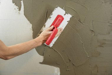 Bir işçi duvarı spatulayla kaplıyor ve çimento karışımı solüsyonu uyguluyor. Tamirci alçıpanı alçıpan üzerine serer. Tamirci evi tamir ediyor. İşçi konutu restore eder. Uzman çatlakları kapatıyor.