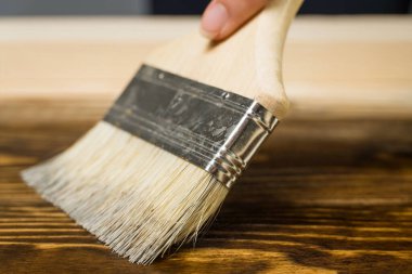 Ahşap desenli kahverengi leke ya da boyayla ahşap bir tablo çizen yakın plan bir boya fırçası. Ahşap işleri, boyama tahtaları.