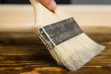 Ahşap desenli kahverengi leke ya da boyayla ahşap bir tablo çizen yakın plan bir boya fırçası. Ahşap işleri, boyama tahtaları.