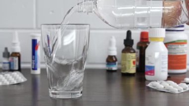 Hapların ve ilaçların arka planına karşı bardağa su dök. Temiz su, sıvı akışı.
