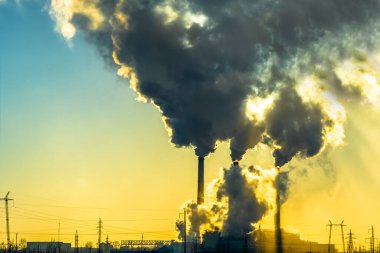 Sanayi kenti üzerinde gün batımı. Fabrika bacaları tütüyor. Çevresel çevre ve atmosfer kirliliği sorunu. İklim değişikliği, çevre felaketi.