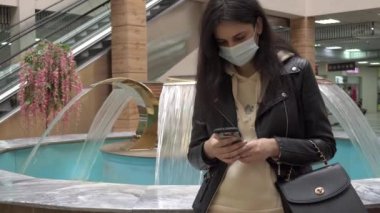 Tıbbi maskeli bir esmer, salgın sırasında çeşmenin yanında durup telefonuna ya da süpermarkete mesaj yazar. Kadın telefonu iletişimi ve mesajlaşması.