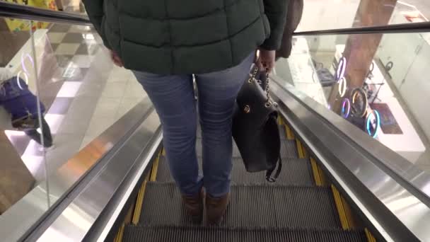 一个女孩在购物中心或超级市场的自动扶梯上下楼 穿着牛仔裤 靴子和钱包的女人的脚在楼下的商店里 超级市场的自动梯和升降机 — 图库视频影像