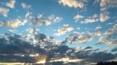 Kara bulutlu gün batımı. Mavi gökyüzü ve beyaz tüy bulutları. Gökyüzünün hareket halindeki manzarası. Güneş ışınları bulutların arasından akşam şafağında kırılıyor.
