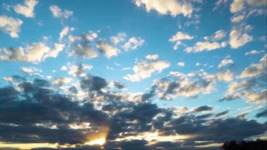 Kara bulutlu gün batımı. Mavi gökyüzü ve beyaz tüy bulutları. Gökyüzünün hareket halindeki manzarası. Güneş ışınları bulutların arasından akşam şafağında kırılıyor.