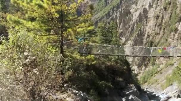 Sherpas y excursionistas caminan un puente que cruza un valle. — Vídeos de Stock