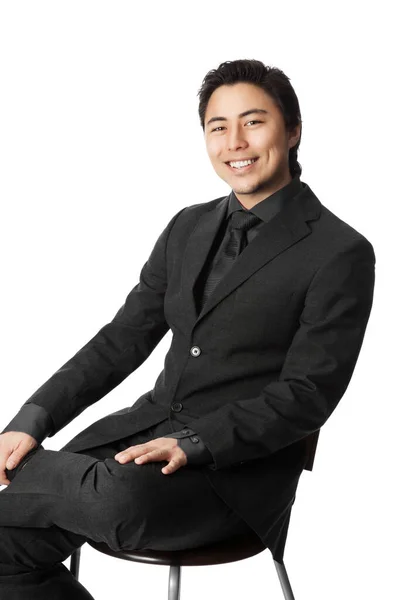 一位英俊的亚洲商人 身穿灰色西装 打着领带 面带微笑地坐在镜头前 白人背景 — 图库照片