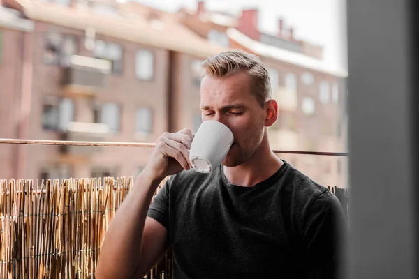 Pensive Blonde Man Sitting Alone His Balcony Drinking Coffee Sunny Royaltyfria Stockfoton