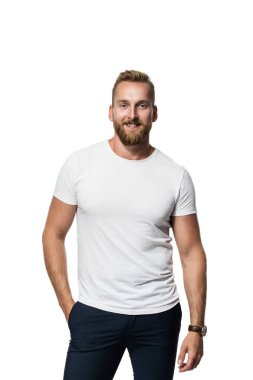 Relaxed attractive blonde bearded man standing against a white background wearing a white t-shirt, smiling towards camera.