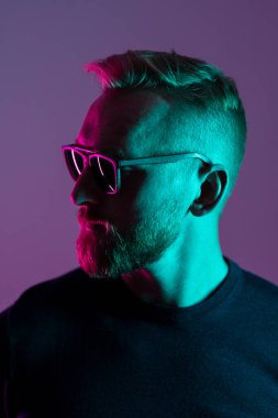 Portrait of a macho man wearing sunglasses looking away from camera. Close up shot with neon lighting.
