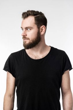 Sakallı, siyah tişörtlü, elleri yana bakan İskandinav bir adam. Gri arkaplan.