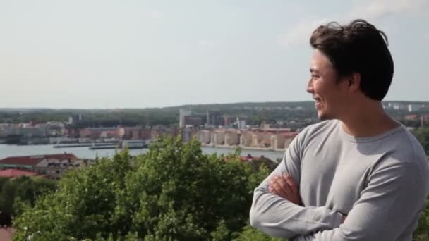 Un hombre asiático de pie sintiéndose genial, llevando una camisa gris frente a un gran paisaje urbano — Vídeos de Stock