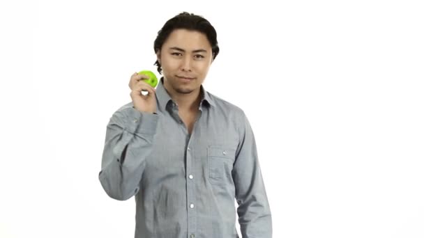 Hombre guapo con una camisa gris sobre un fondo blanco sosteniendo una manzana verde — Vídeo de stock