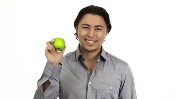 Hombre guapo con una camisa gris sobre un fondo blanco sosteniendo una manzana verde — Vídeos de Stock