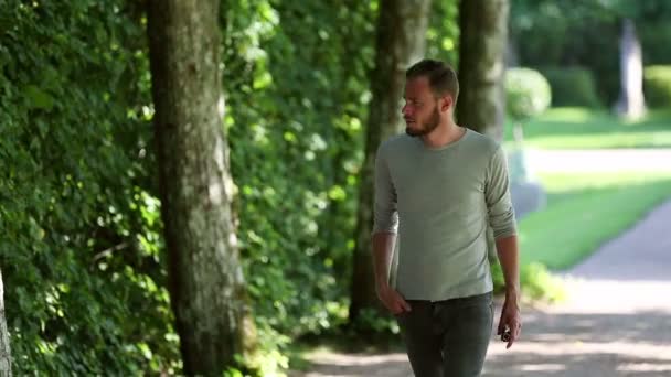 Дорослий у сірій сорочці, що йде стежкою надворі — стокове відео