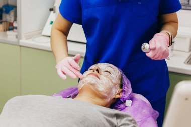 Kozmetik uzmanı hastanın yüzüne anestezi ile krem sürüyor. Portre yakın çekim görüntüsü. Lazer cilt yenileme hazırlığı