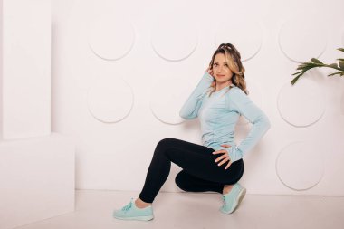 Spor kıyafetli zayıf genç bir kadın, mutlu, neşeli. Spor kıyafetleri içinde gülümseyen mutlu genç bir kadın. Beyaz arkaplandaki kaslı fitness modeli kopyalama alanına bakıyor.