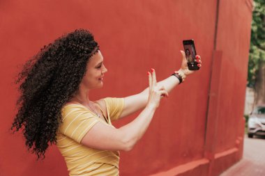 Saçları kıvırcık, güzel gülümseyen bir model selfie çekiyor.