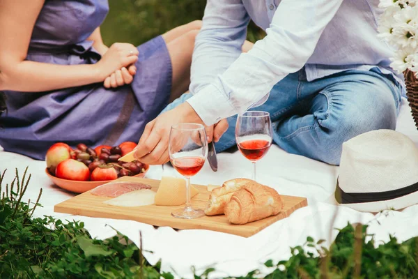 Romantic dinner outdoors. Glasses with red wine, grapes and cheese on wooden board.