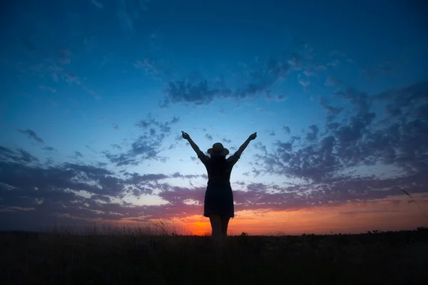 帽子をかぶった孤独な女性が夏の夕暮れ時に空に手を上げて草の中に滞在します 曇り空に — ストック写真