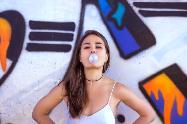 Duvarın arkasında duvar yazısı olan bir kadın bir sakız balonunu şişiriyor.