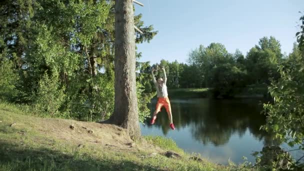 Chlapec v létě skočí na bungee u jezera. Teenager na břehu rybníka hraje bungee — Stock video
