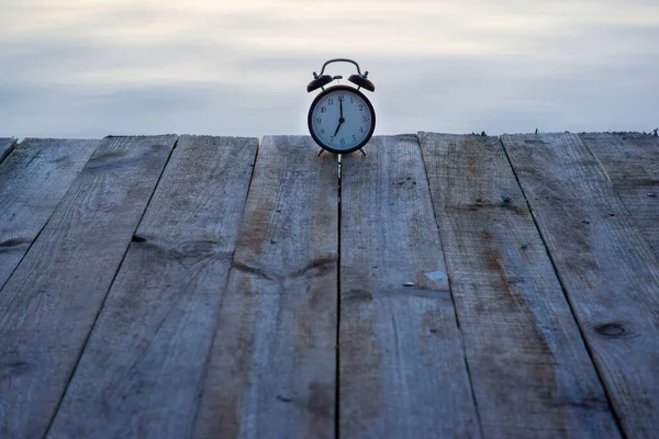 Concepto horario de verano. Reloj despertador en puente de madera sobre fondo de salida del sol del mar —  Fotos de Stock