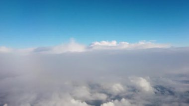 4K uçak görüntüsü bulutların üzerinde açık mavi gökyüzü ile uçuyor.