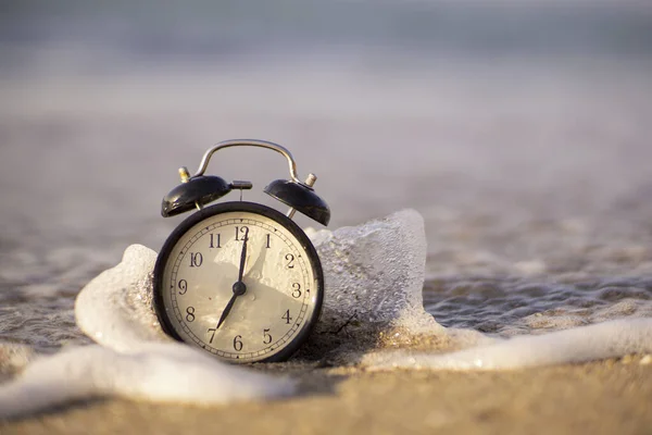 Alarm clock splashing in the beach water — Stock Photo, Image