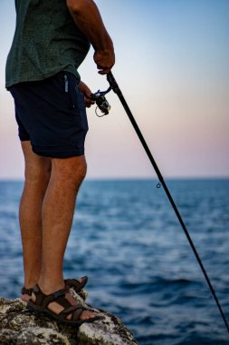 Deniz kıyısında gün batımında kayalık balık tutan adam..