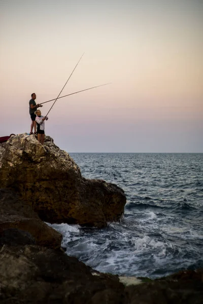 男人和女人在SUNSET海岸海岸的岩石上钓鱼. — 图库照片