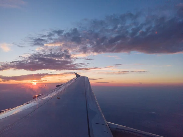 SUNSET ABOVE THE SKY VIEWED INFLIGHT FROM AN AIRPLANE WINDOW WITH THE WING IN THE FOREGROUND — Stock Photo, Image