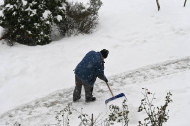 Soğuk bir kış gününde, özel bir küreği olan bir adam bütün gün yağan bir kar yolunu temizler..