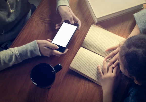 Girl reading a book and another girl holding smart phone