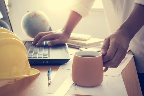 Mains de l'architecte tenant une tasse de café et travaillant sur un ordinateur portable — Photo