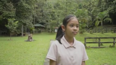 Yaz tatili boyunca Forest Park 'ın çimlerinde rahatça yürüyen tatlı Asyalı kız. Tropikal orman manzarasını izlerken gülümseyen mutlu genç kız. Tayland.