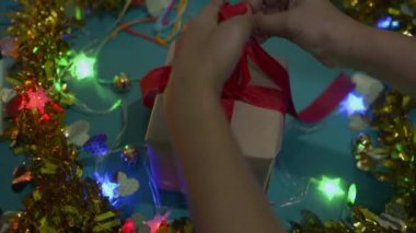 Kadın eli masaya sarılı Noel hediyesini tamamlar. Kadın hediye kutusunu paketliyor ve kırmızı kurdeleyi fiyonkla bağlıyor. Yılbaşı ve Noel tatiline hazırlanıyor.