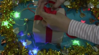 Kadın eli masaya sarılı Noel hediyesini tamamlar. Kadın hediye kutusunu paketliyor ve kırmızı kurdeleyi fiyonkla bağlıyor. Yılbaşı ve Noel tatiline hazırlanıyor.