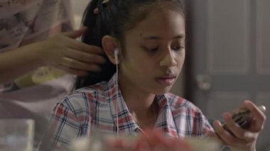 Anne, kızı için örgü örüyor. Evde saçlarını tararken cep telefonuyla film izleyen sevimli bir kız..