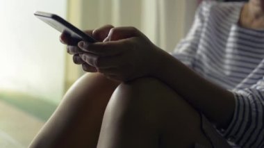 Günlük elbiseli bir kadın evinin kapısında oturmuş cep telefonundan iletişim kurmak ve internette sohbet etmek için mesaj atıyor. Modern teknolojiye sahip insanlar.