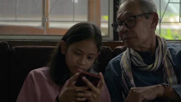 재밌는 노인이 거실에서 귀여운 손녀와 휴대폰으로 게임을 사이의 시간을 보내는 — 비디오