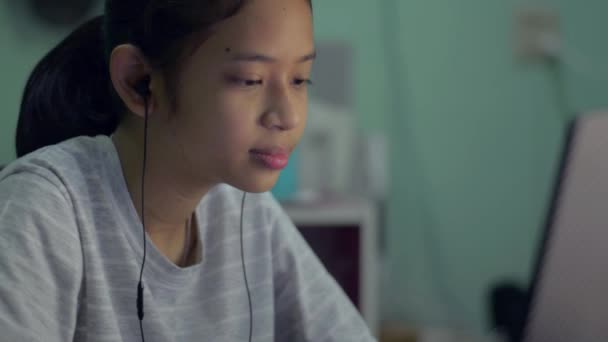 可爱的亚洲女孩带着耳机 在家里通过笔记本电脑上的视频通话与她的朋友交谈 用电脑摄像头聊天做笔记 远程通信 — 图库视频影像
