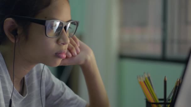 自宅でオンライン学習中にコンピュータのラップトップモニターを見てイヤフォンを身に着けて眼鏡で愛らしいアジアの女の子の側面のビューを閉じます 教育のためのインターネット技術 — ストック動画