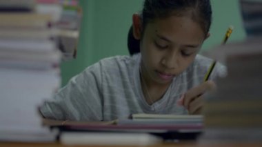Asyalı kız lisesi masa başında kitap yığınıyla ödev yapıyor. Genç kız evde bir sürü işi olan sıkılmış bir yüz ifadesi sergiliyor. Evde çalış.. 