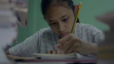 Geceleri masanın üstünde bir yığın kitapla ödev yapan ciddi bir genç kız. Dişi ergen, evde çok işi olduğu için yorgunluğunu ifade ediyor..