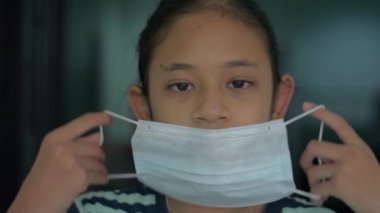 Koronavirüs salgınını önlemek için koruyucu maske takan sevimli Asyalı bir kızın portresi. Diğer insanları korumak için solunum cihazını tak. Salgın COVID-19 kavramı.