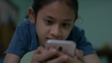 Sevimli Taylandlı kız cep telefonundan sosyal medya mesajları ve mesajlar okumayı seviyor. Genç kız yatakta uzanıyor ve dinleniyor ve gece akıllı telefon kullanıyor..