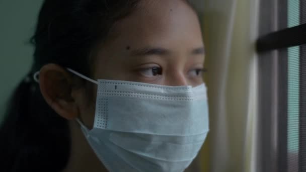 不快乐的亚洲女孩 在家里被隔离时 戴着防护面罩 从窗户往外看 科罗纳威斯大流行病Covid 19局势安全 — 图库视频影像