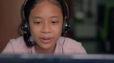 Kulaklık takan sevimli Asyalı kız portresi evde dizüstü bilgisayardan ders çalışırken uzaktan öğretmenle iletişim kurdu. Video çağrı teknolojisi.